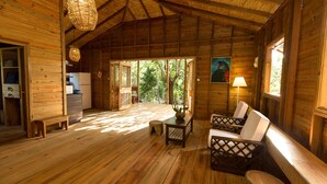 A wooden cabin with a dining area, a kitchen, and a large window overlooking the forest. - BAYLEAF: The Perfect Hideaway near secluded beach (Hellene)