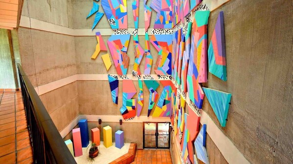 Una escalera con arte mural geométrico colorido y una planta en el rellano.