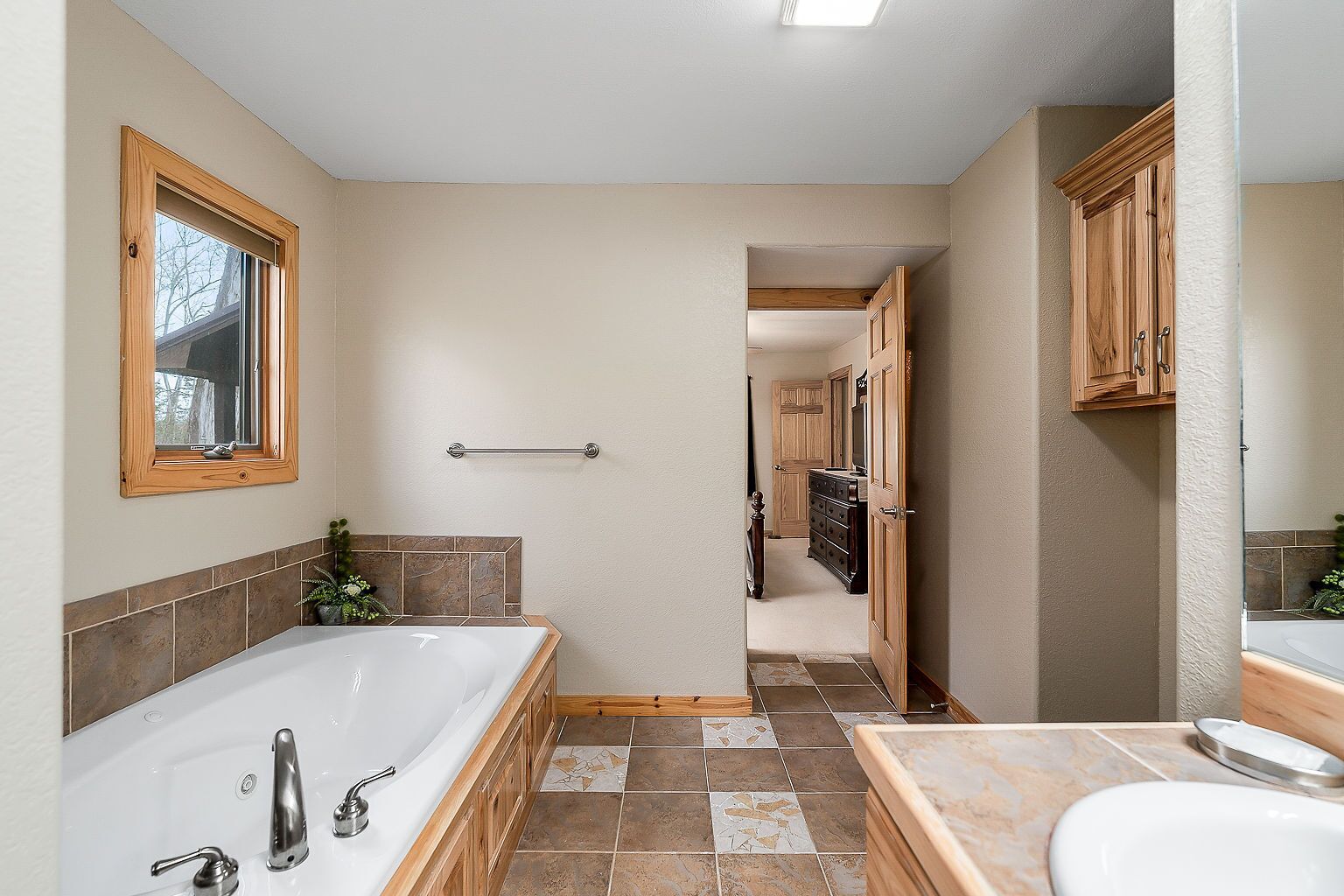 A bathroom with a large bathtub, a sink, and a mirror. There is a wooden cabinet and a towel rack.