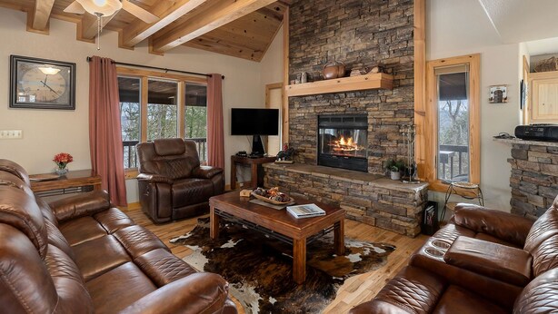 A cozy living room with leather sofas, a stone fireplace, and a ceiling fan.