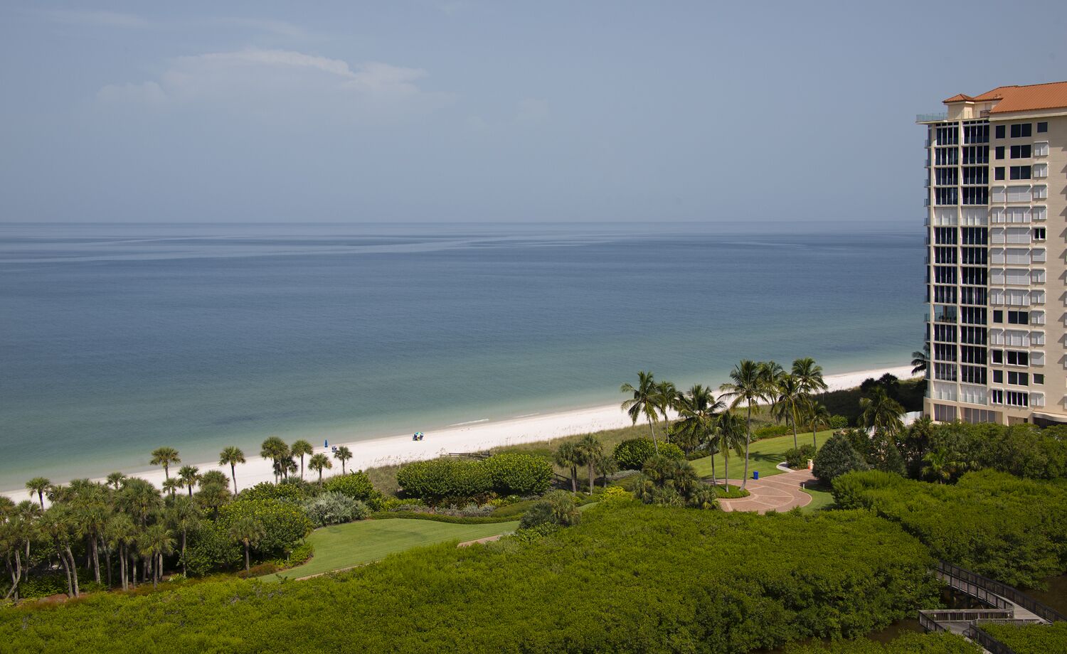 Ett hotell vid stranden med utsikt över havet, en sandstrand och palmer.