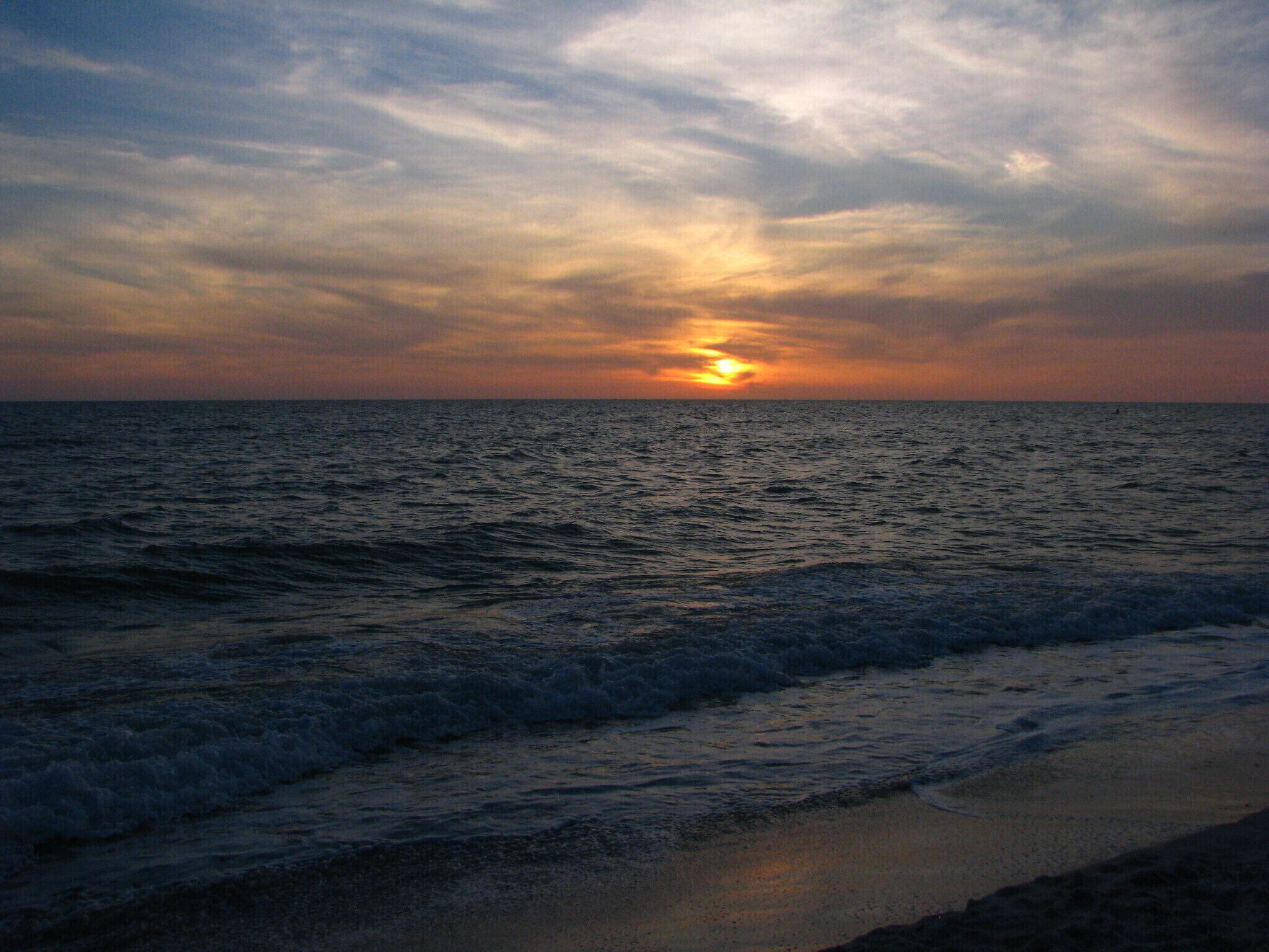 A sunset over the ocean with waves approaching the shore.