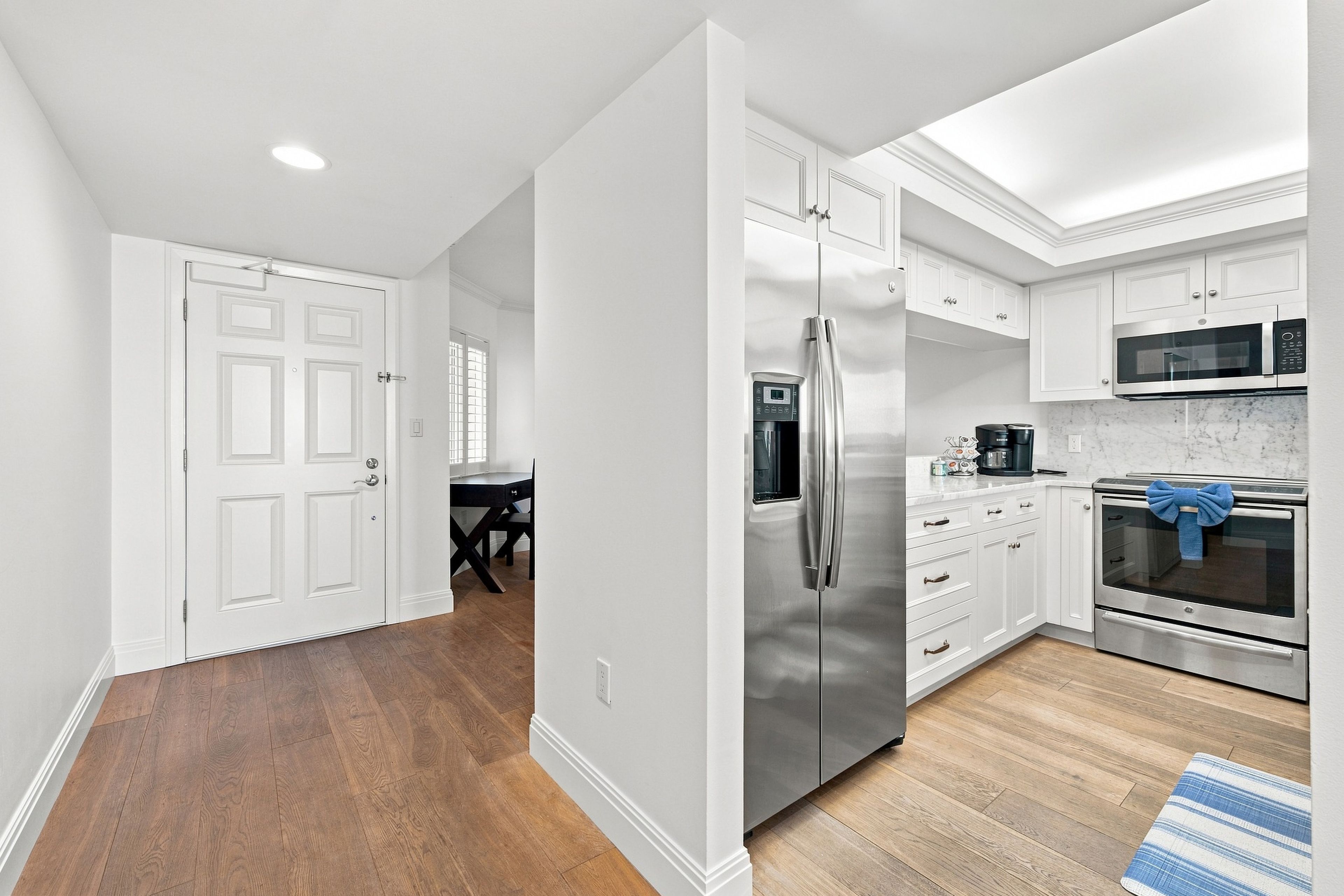 A modern kitchen with stainless steel appliances, white cabinetry, and a wooden floor.