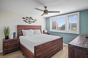 Un dormitorio con cama de madera, ventilador de techo, ventana con persianas y una decoración de peces en la pared.