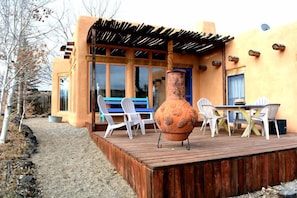 Una terraza de madera con una mesa y sillas, una maceta de terracota grande y un edificio de estilo arquitectónico único.
