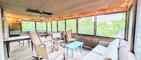 Un área de estar al aire libre con muebles de madera, ventilador de techo y luces colgantes.