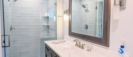 A modern bathroom with a glass-enclosed shower, a large mirror, and a white vanity with dark cabinets.