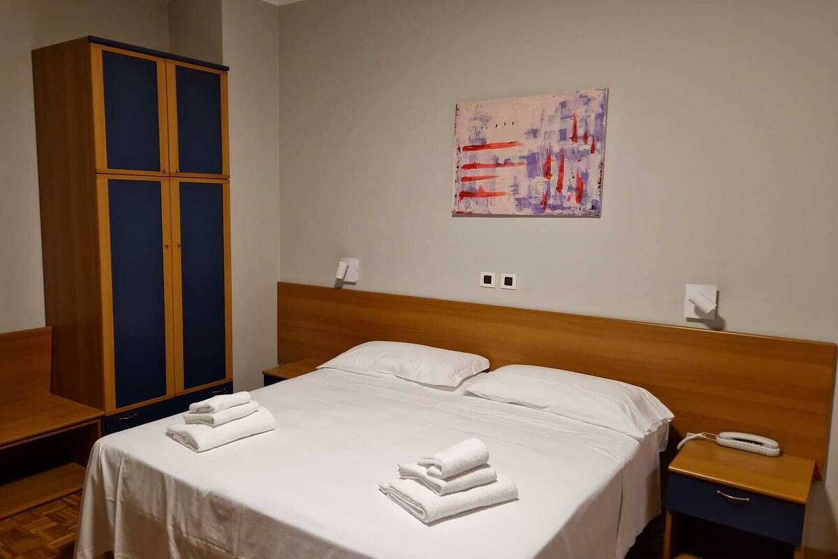 Et hotelværelse med en seng, et klædeskab, et natbord og et billede på væggen.