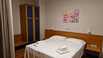 Una habitación de hotel con cama, armario, mesita de noche y un cuadro en la pared.