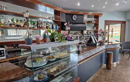 A bar area with a glass display case containing food items, a bar counter with a clock, and shelves with bottles.