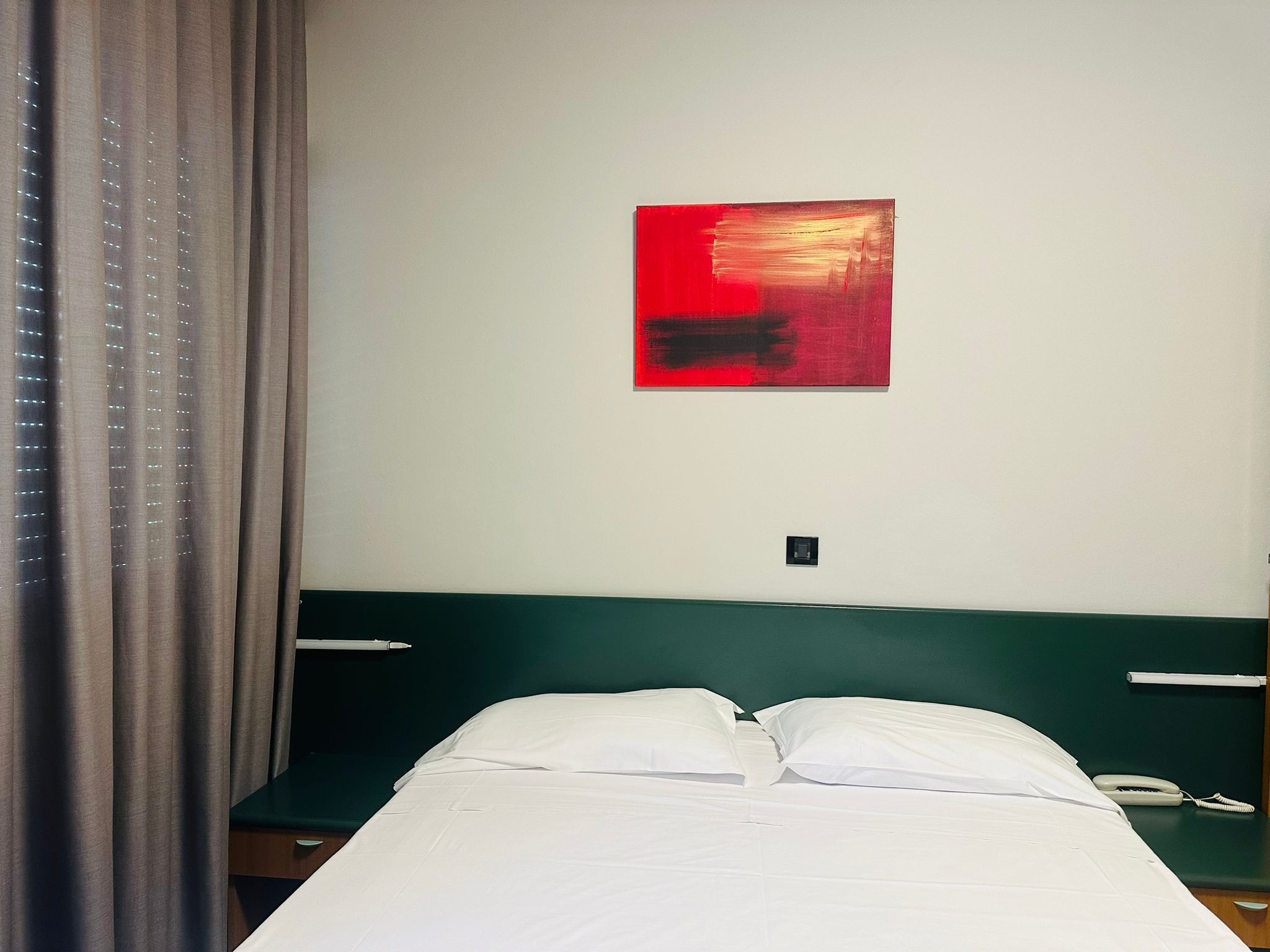 Une chambre d’hôtel avec un lit, un tableau accroché au mur, un téléphone et une tête de lit verte.