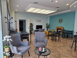 Un vestíbulo amplio con sillones grises, una chimenea y un comedor con varias mesas y sillas.