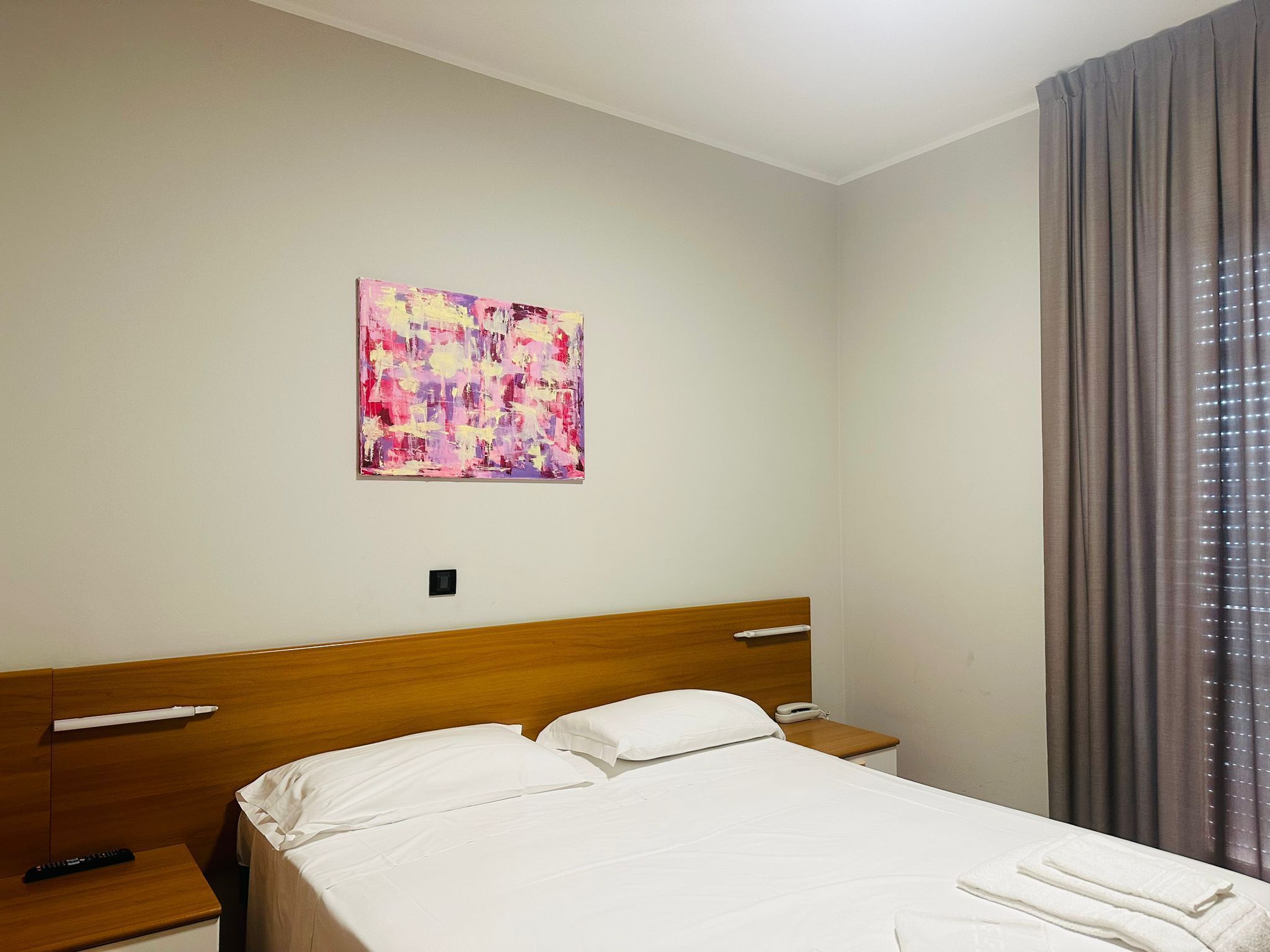 Ein Hotelzimmer mit einem hölzernen Kopfende, einem Bett mit weißer Bettwäsche, einem Nachttisch mit Telefon und einem Gemälde an der Wand.