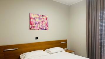 Ein Hotelzimmer mit einem hölzernen Kopfende, einem Bett mit weißer Bettwäsche, einem Nachttisch mit Telefon und einem Gemälde an der Wand.
