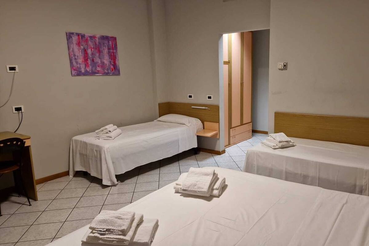 Et hotelværelse med to senge, et træskab, et lille bord og et billede på væggen.