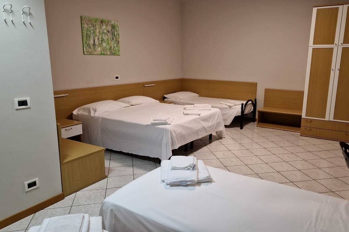 Et hotelværelse med to senge, et træskab, et lille bord og et billede på væggen.
