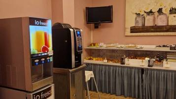 Una kitchenette con cafetera, televisor y mesas de buffet.