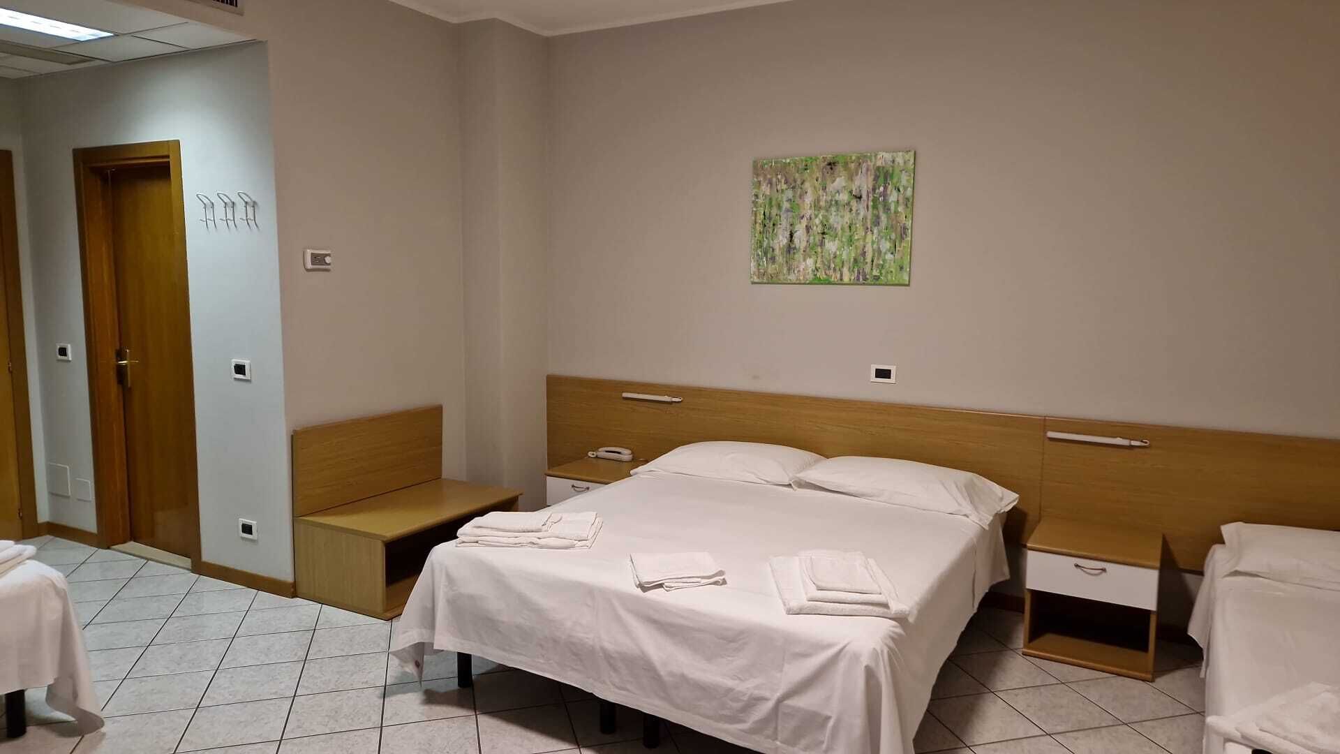 Una habitación de hotel con una cama, mesitas de noche, un banco y un cuadro en la pared.