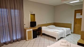 Habitación de hotel con cama, escritorio con computadora, una silla, televisor y ventana con cortinas.