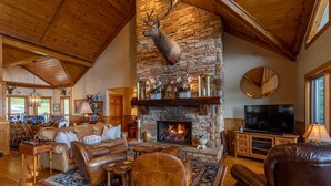 A cozy living room with a stone fireplace, leather furniture, and a mounted deer head. - The Boulders: 5 Suites | Hot Tub | 50mi Views | Pool Table | Sauna | Wet Bar | Dog Friendly! (Boone)