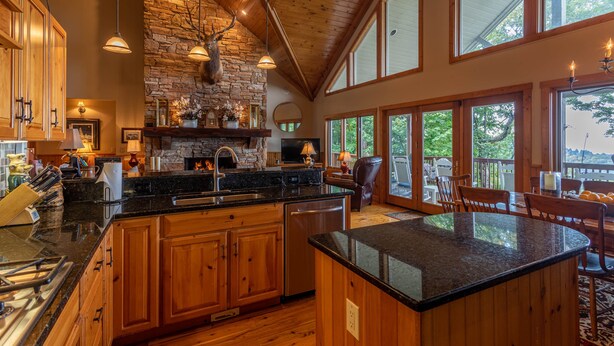 A spacious kitchen with wooden cabinets, a stone fireplace, and a large island. - The Boulders: 5 Suites | Hot Tub | 50mi Views | Pool Table | Sauna | Wet Bar | Dog Friendly! (Boone)