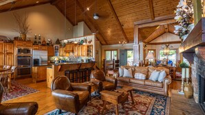 A spacious living area with a fireplace, leather furniture, and a kitchen with wooden cabinets and a bar. - The Boulders: 5 Suites | Hot Tub | 50mi Views | Pool Table | Sauna | Wet Bar | Dog Friendly! (Boone)