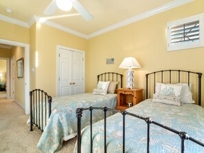 A bedroom with two beds, a ceiling fan, a nightstand with a lamp, and a door with a sign.