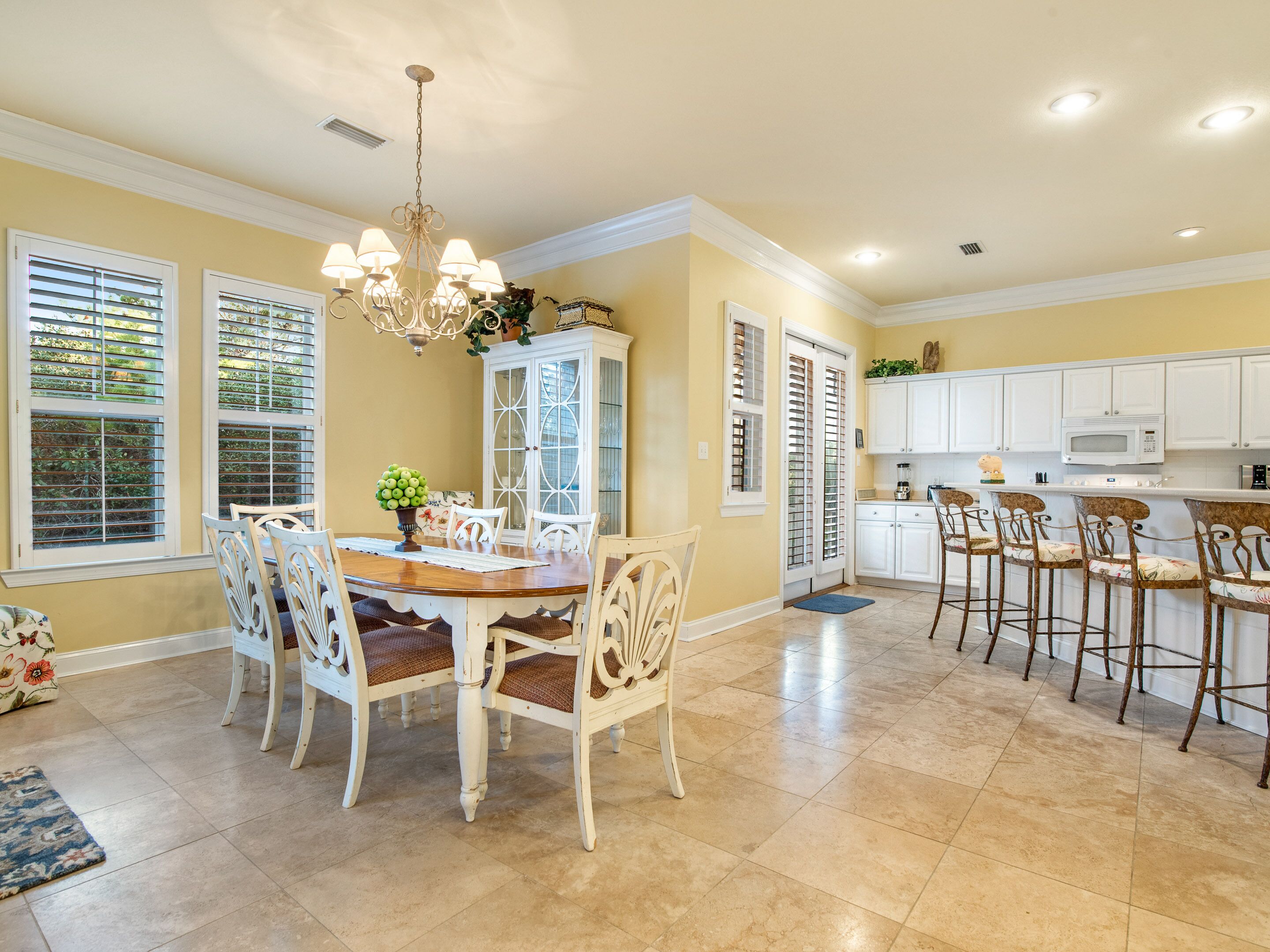 A spacious kitchen with white cabinets, a dining area with a wooden table and white chairs, and a chandelier.