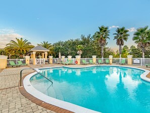 A swimming pool with lounge chairs and a gazebo, surrounded by palm trees and a white fence.