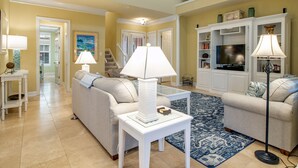 A spacious living room with a high ceiling, a staircase, and a view of the upper floor.