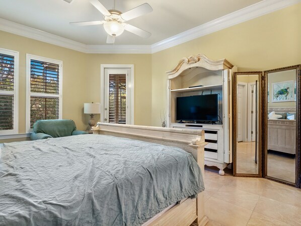 A bedroom with a bed, a television on a stand, a ceiling fan, and a large mirror.