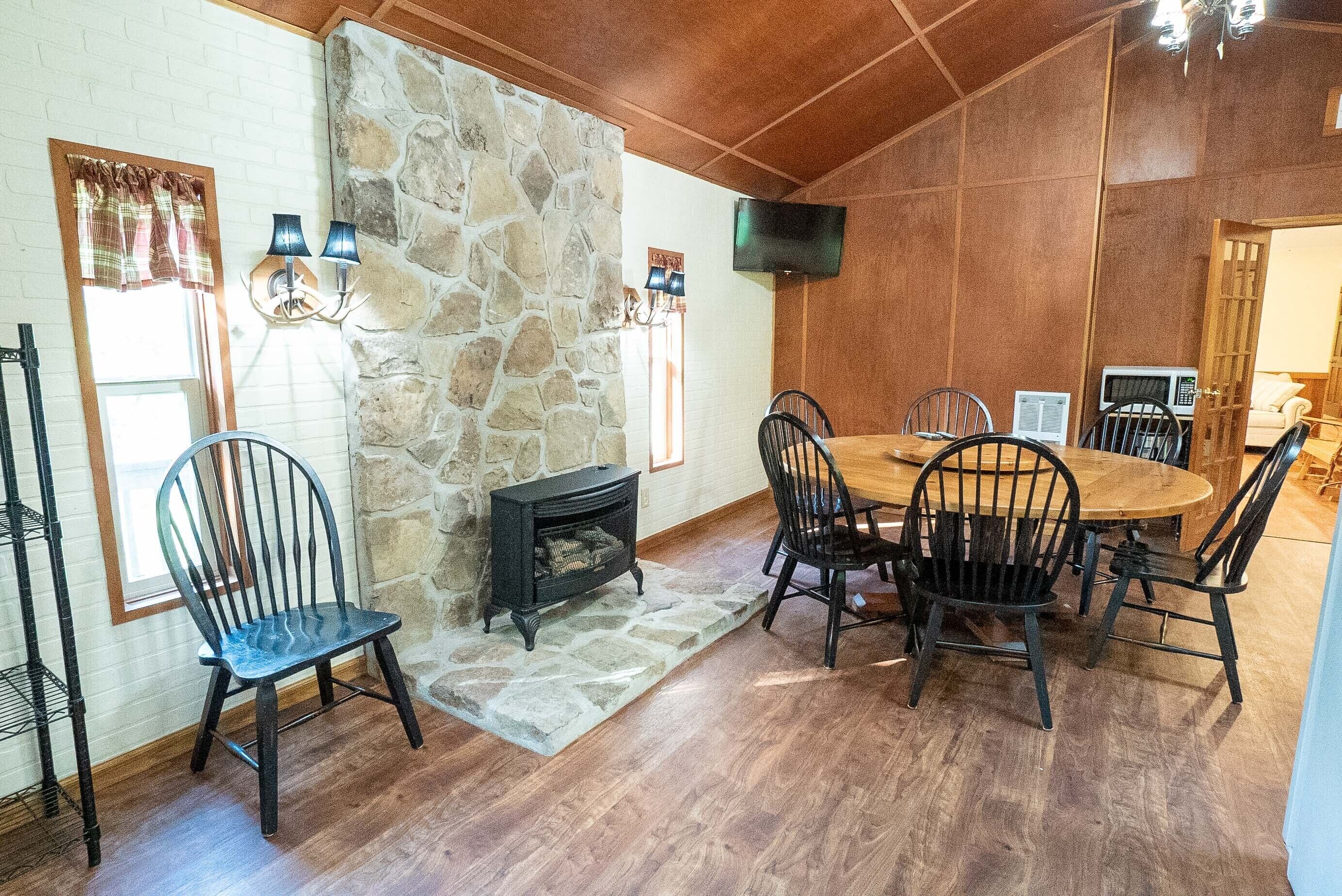 A dining area with a stone wall, wooden ceiling, and a fireplace.