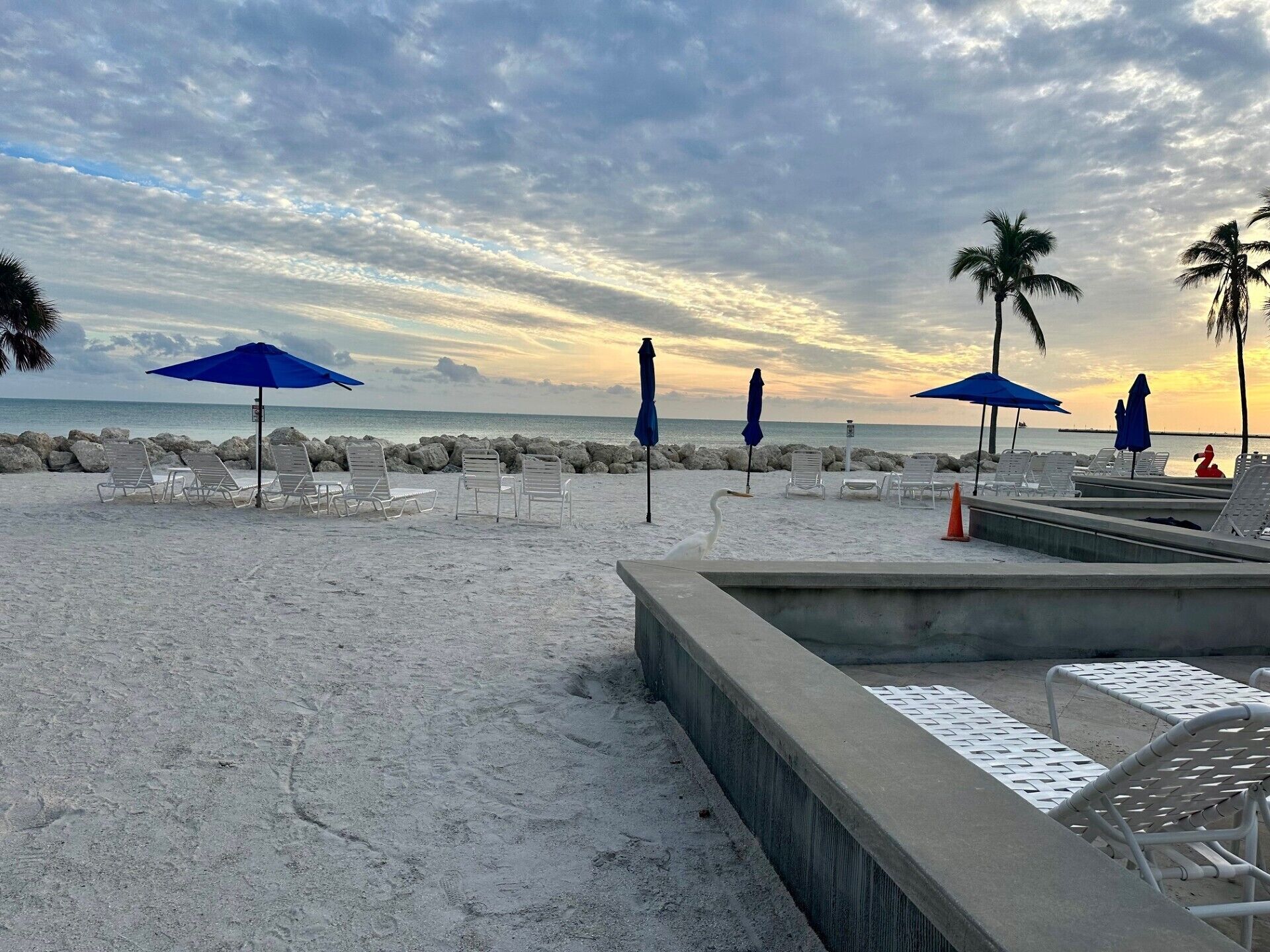 Une plage avec des chaises longues et des parasols, une promenade en béton et une côte rocheuse.