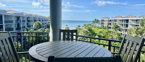 A balcony with a round table and chairs, overlooking a beach and hotel buildings.