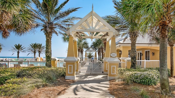 A gated entrance with a white fence, palm trees, and a clear sky.