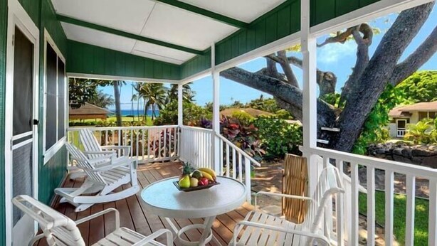 A covered outdoor area with a table and chairs, a view of a tropical landscape, and a large tree.