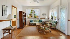 A room with a ceiling fan, a sofa, two chairs, a small table, and a bookshelf.