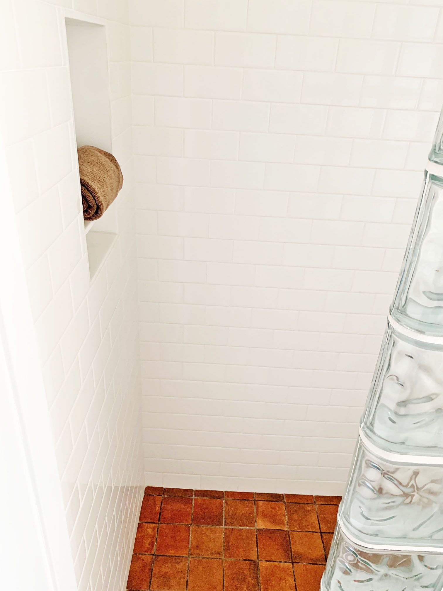 A bathroom with white tiled walls, a brown tiled floor, and a glass shower enclosure.