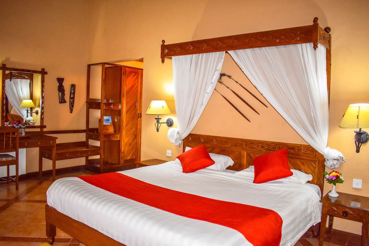 A four-poster bed with a canopy, a wooden desk with a chair, and a mirror.