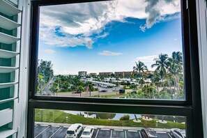 Une vue à travers une fenêtre, avec un ciel dégagé, des palmiers et un parking.