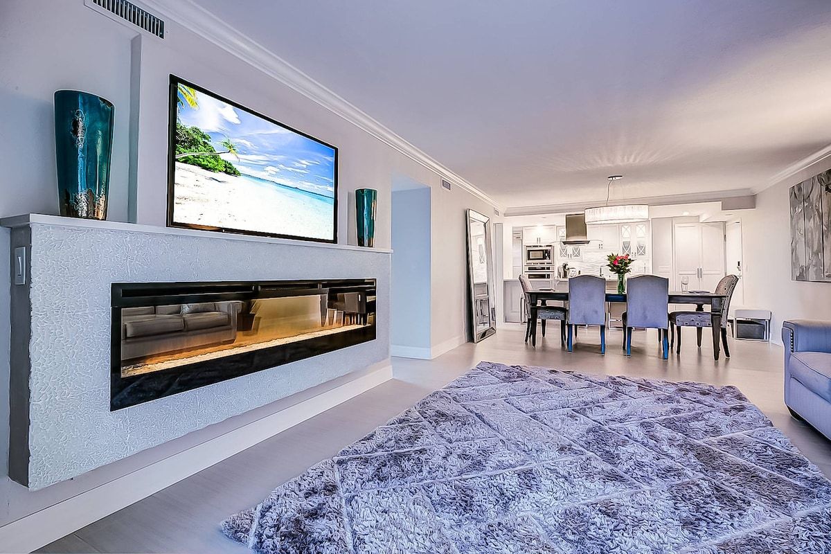 A modern living room with a fireplace, a flat-screen TV, and a dining area with chairs and a table.