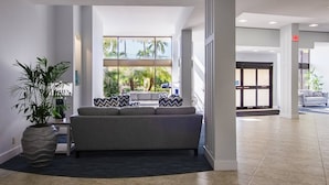 A modern lobby with a grey sofa, a large potted plant, and a view of palm trees through large windows. - Expansive Renovated Condo, Heated Pools, Tennis, Fishing on Intracoastal | Siesta Key Beach (Siesta Key)