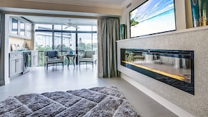 A modern living room with a fireplace, large windows, and a view of the outdoors. - Expansive Renovated Condo, Heated Pools, Tennis, Fishing on Intracoastal | Siesta Key Beach (Siesta Key)