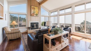A spacious living room with a fireplace, large windows, and a balcony. - Pet-Friendly Home on Lodge Hill in Cambria Offers the Best Ocean Views! (Cambria)