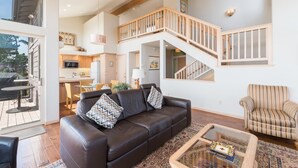 A spacious living area with a brown leather sofa, a striped armchair, and a coffee table. A staircase leads to an upper level with a balcony. - Pet-Friendly Home on Lodge Hill in Cambria Offers the Best Ocean Views! (Cambria)
