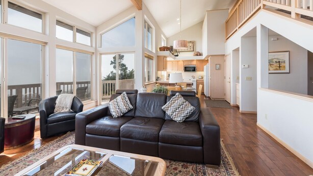 A spacious living area with a leather sofa, a glass coffee table, and a view of the kitchen and balcony. - Pet-Friendly Home on Lodge Hill in Cambria Offers the Best Ocean Views! (Cambria)