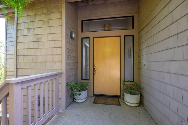 A wooden front door with a glass panel, two potted plants, and a white railing. - Pet-Friendly Home on Lodge Hill in Cambria Offers the Best Ocean Views! (Cambria)
