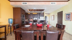 A dining area with a wooden table and chairs, a water dispenser, and kitchen cabinets in the background.