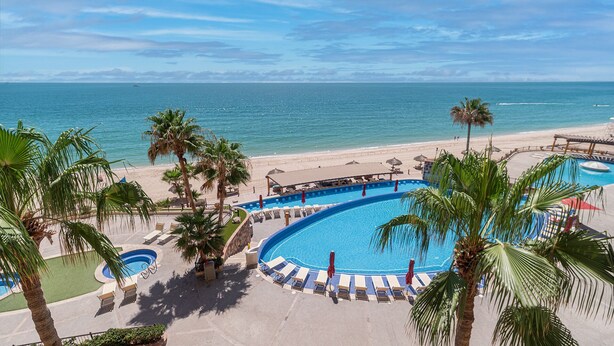 A resort with a large pool, palm trees, and a beach view.