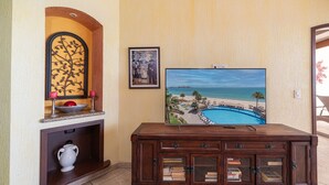 A living room with a TV displaying a beach scene, a fireplace, a decorative wall piece, and a wooden cabinet with books.